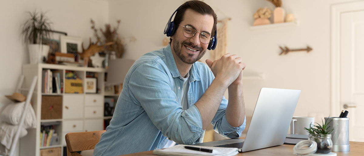 Junger, Mann, sitzt, Schreibtisch, arbeiten, Online, Seminar, Webinar, Onlineseminar, zuhören, lächeln