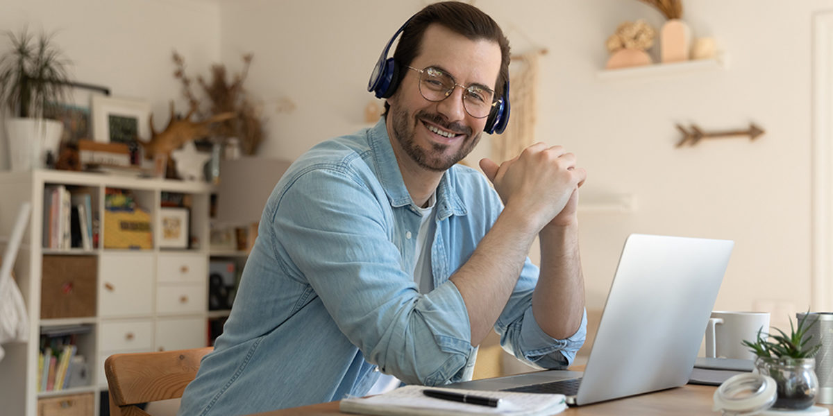 Junger, Mann, sitzt, Schreibtisch, arbeiten, Online, Seminar, Webinar, Onlineseminar, zuhören, lächeln
