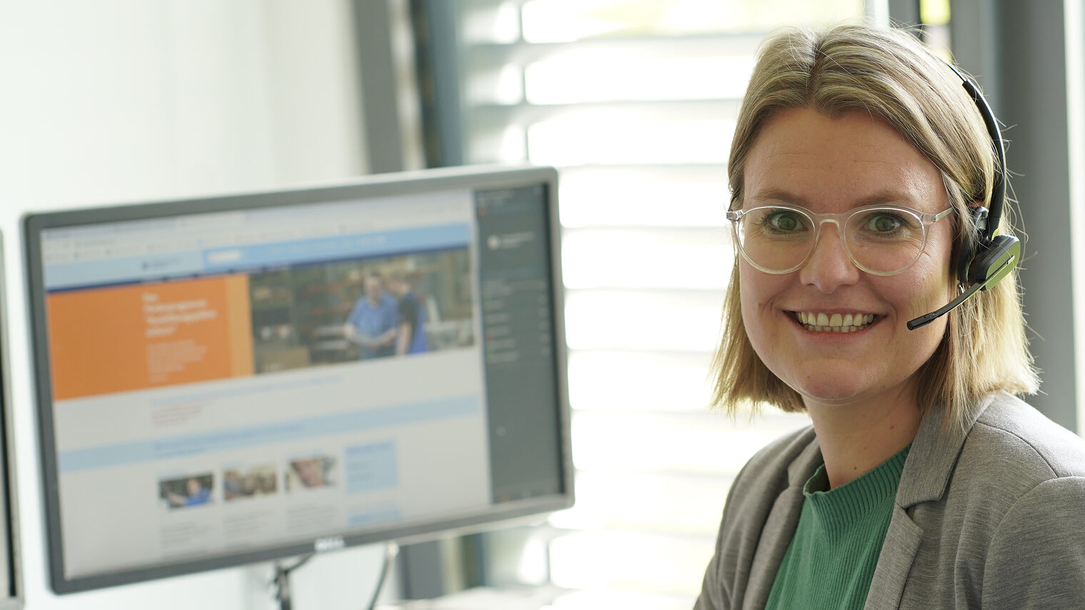 Anja Kloos sitzt vor dem PC in ihrem Büro und lächelt in die Kammera.