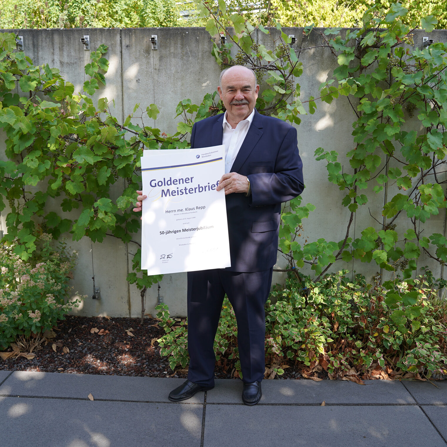 Klaus Repp, Meister im Metallbauerhandwerk und Ehrenpräsident der Handwerkskammer Wiesbaden, hält seinen zuvor erhaltenen Goldenen Meisterbrief in der Hand.