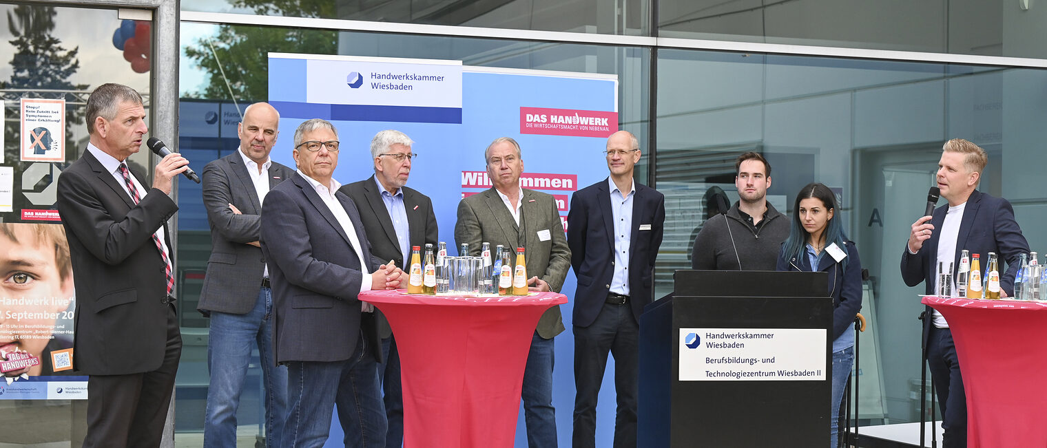 Das Bild zeigt die von Kai Völker, vom Hessischen Rundfunk, moderierten Talkrunde mit Landrat Frank Kilian, Oberbürgermeister Gert-Uwe Mende, dem Geschäftsführer der Agentur für Arbeit Wiesbaden, Stephen Spieker, Kammerpräsident Stefan Füll, Hauptgeschäftsführer Bernhard Mundschenk und Kreishandwerksmeister Holger Balz vor dem Eingang des Berufsbildungs- und Technologiezentrum.