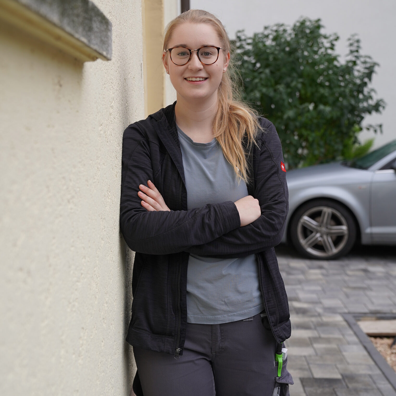 Caroline Schäfer ist Lehrling des Monats. Die junge Frau mit blonden langen Haaren und Brille lehnt an Hausmauer und blickt freundlich in die Kamera.