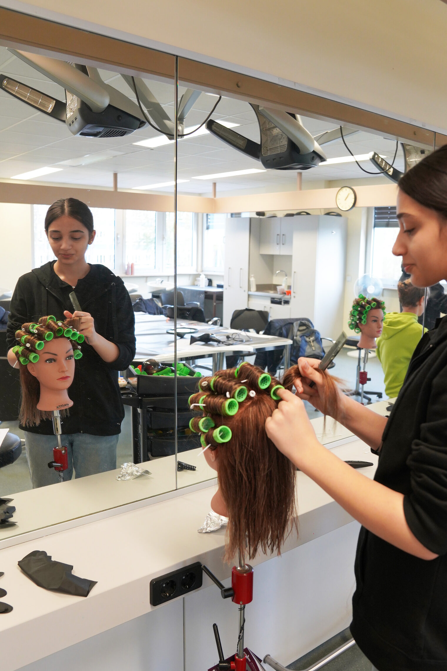 Eine Schülerin besucht die Berufsorientierungswoche und ist in der Friseur-Lehrwerkstatt. Die Aufgabe ist, Lockenwickler auf einen Übungskopf einzudrehen.