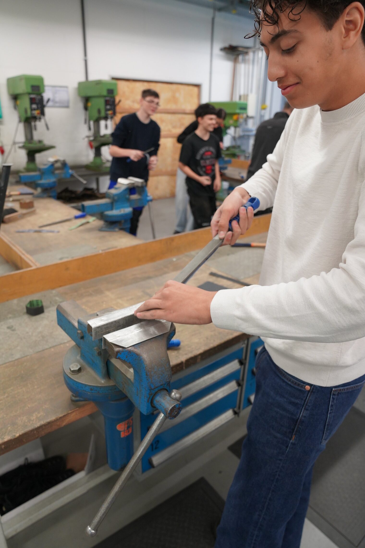 Ein Schüler besucht die Berufsorientierungswoche und ist in der Metall-Lehrwerkstatt. Die Aufgabe besteht darin, einen Würfel herzustellen. Auf dem Bild ist er an der Werkbank und schleift den eingespannten Würfel. 