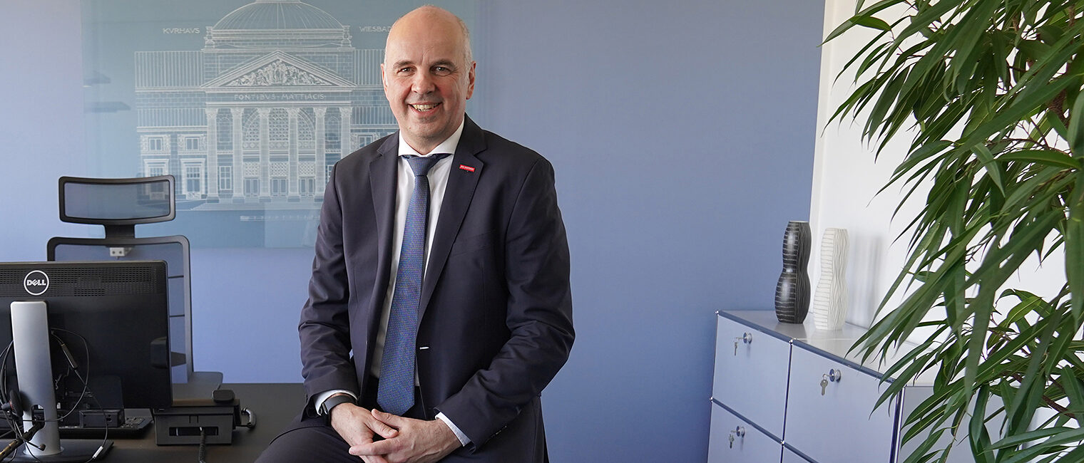 Portrait von Stefan Füll Präsident des Hessischen Handwerkstages, in dunklem Anzug halb sitzend auf der Schreibtischkante in seinem Büro