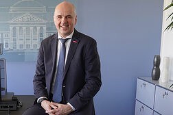 Portrait von Stefan Füll Präsident des Hessischen Handwerkstages, in dunklem Anzug halb sitzend auf der Schreibtischkante in seinem Büro