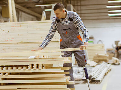 Ein Mitarbeiter, der eine Beinprotese hat, greift nach einer Holzlatte in einer großen Holzwerkstatt.