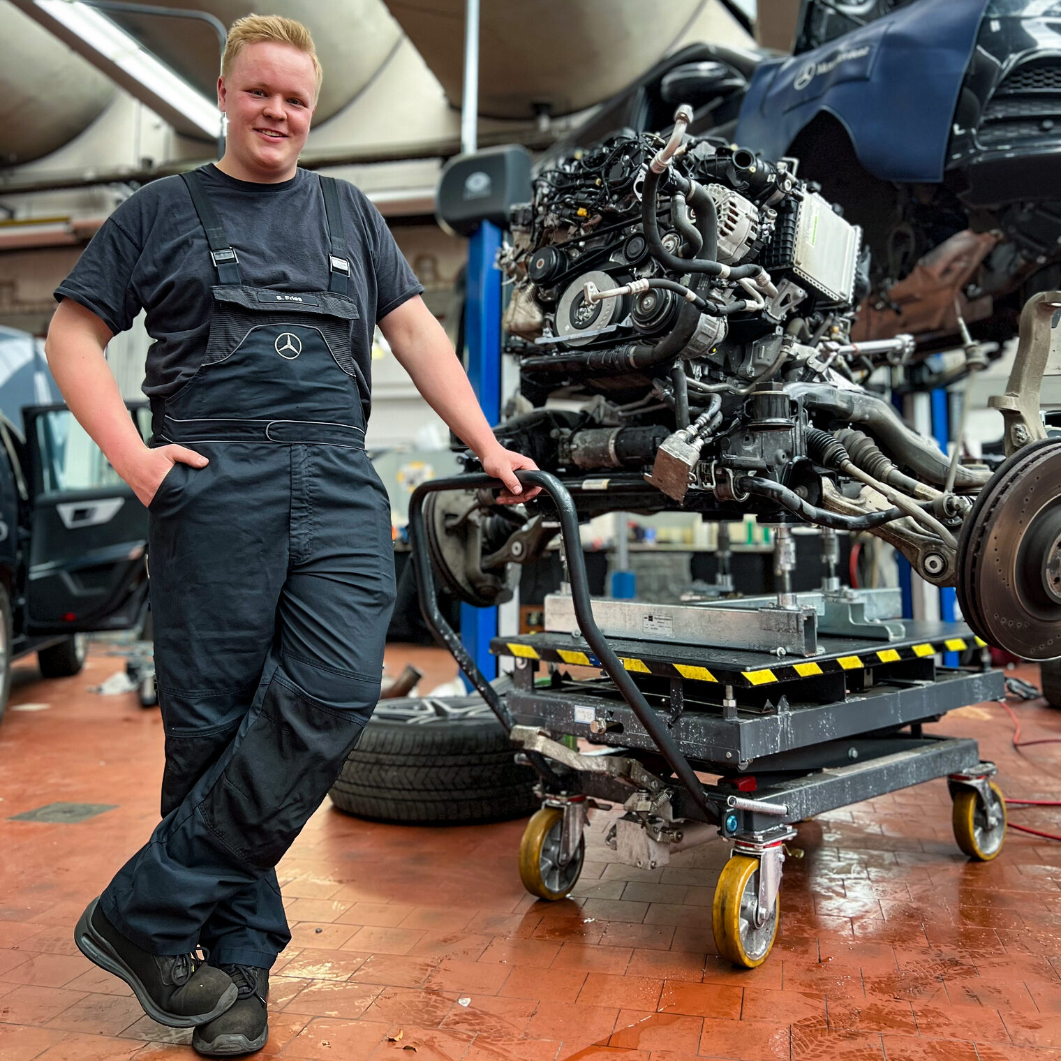 Das Bild zeigt den Lehrling des Monats März 2023, Sören Fries, der bei der Firma Neils & Kraft in Gießen zum Kraftfahrzeugmechatroniker ausgebildet wird, in der Werkstatt an einem ausgebauten Motorblock. 