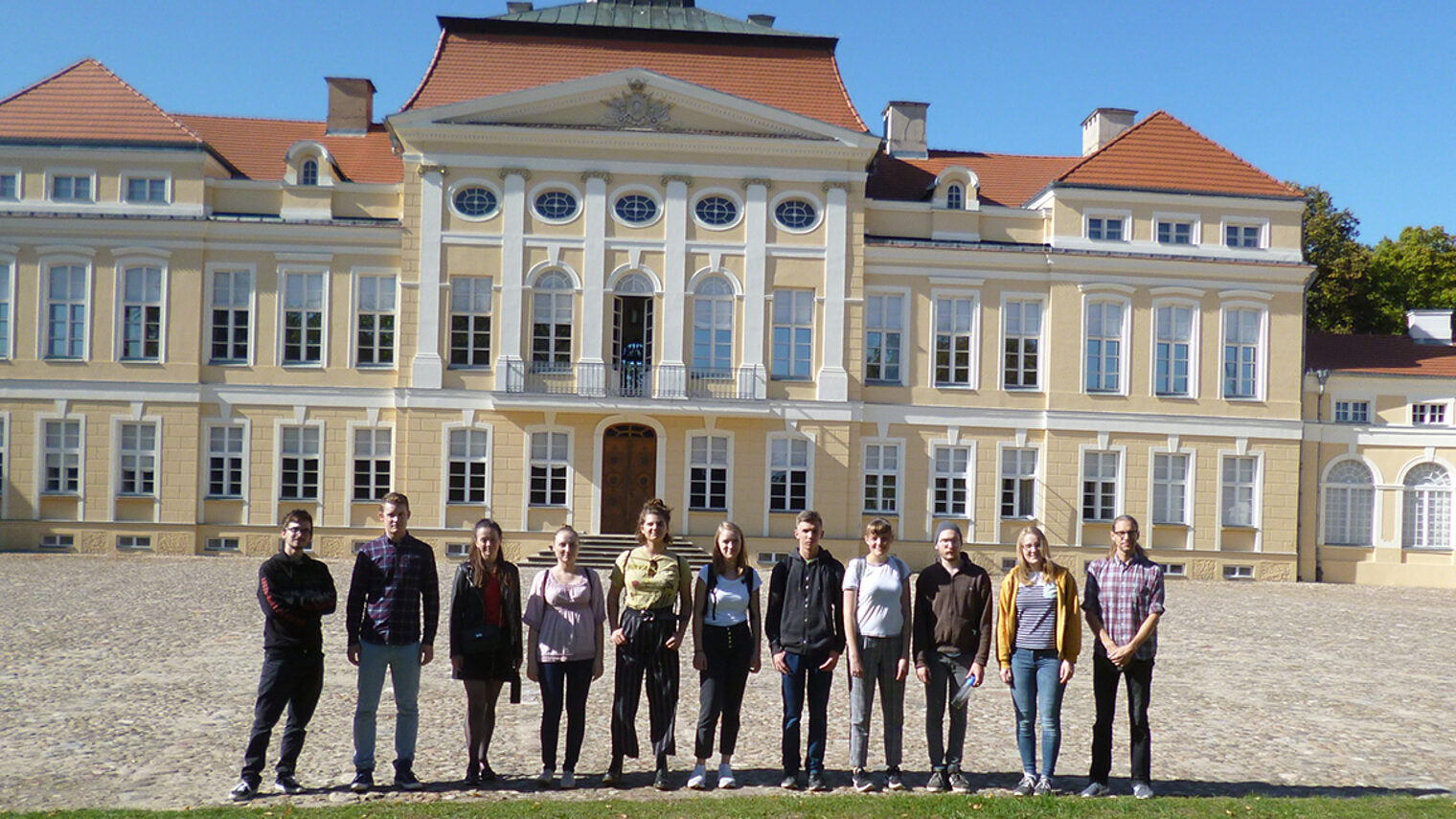 Gruppenfoto von Jugendlichen die nebeneinander stehen. in der Außenanlage vor einem großen historischen Gebäude in Posen.