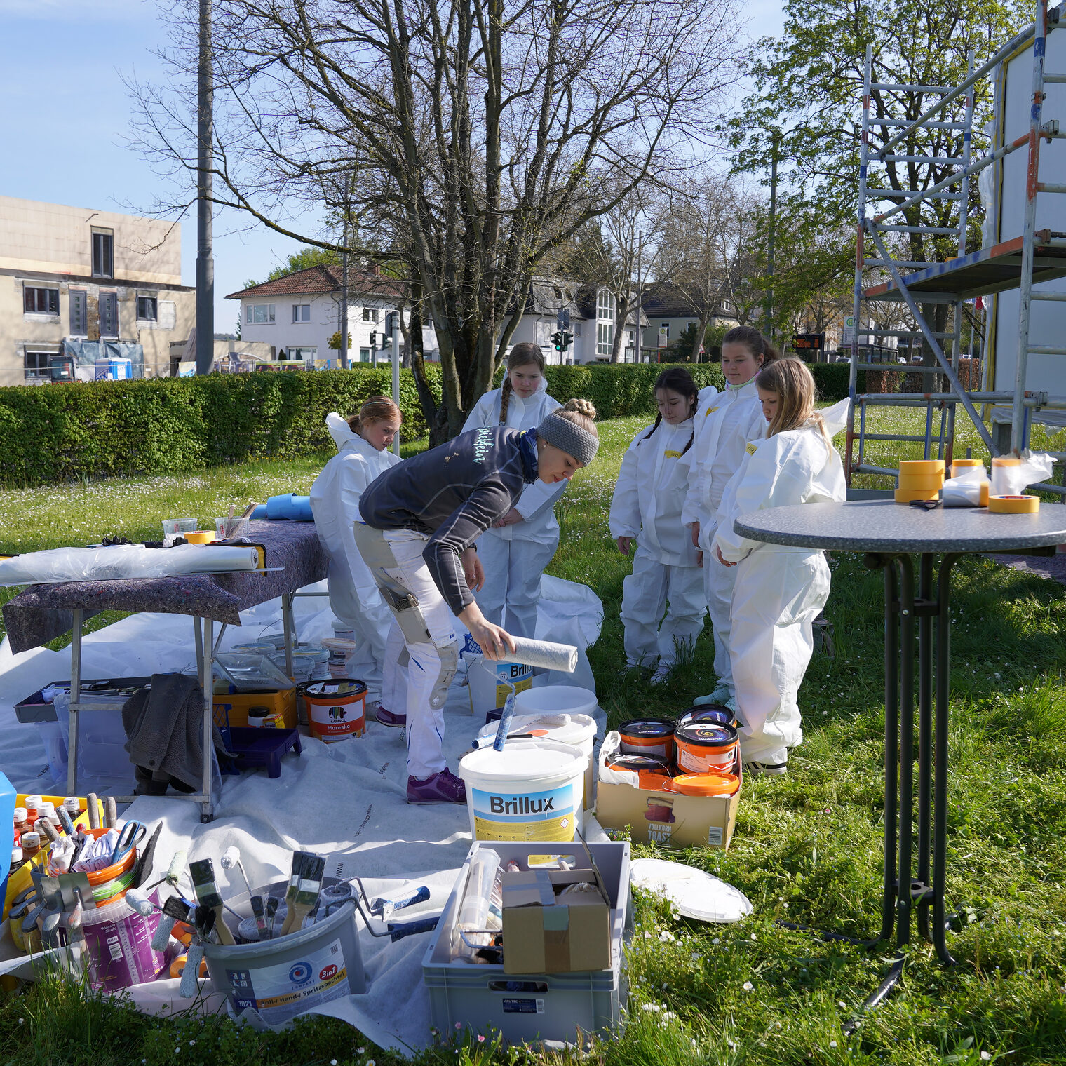 Malermeisterin Jessica Jörges und eine kleine Gruppe Mädchen in Maleranzügen bereiten Farbe und Werkzeug für Malerarbeiten vor.