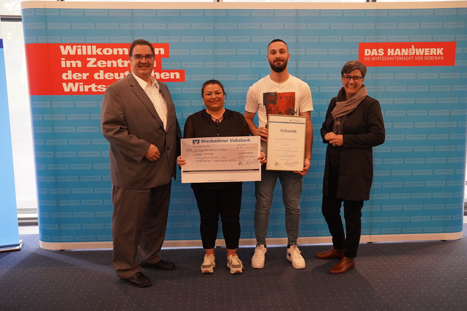 Gruppenfoto bei Scheck und Urkundenübergabe des Hessischen Integrationspreises 2023 an die Firma Haar Lounge.