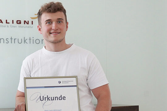 Profilbild von Lars Altmayer. Freundlich lächelnder junger Mann in weißem T-Shirt mit kurz geschnittenen gelockten Haaren