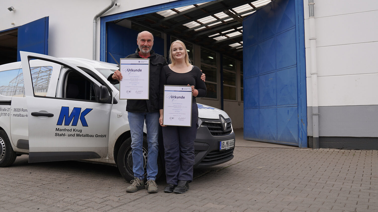 Ina Weckesser, Lehrling des Monats Juni 2023, und Geschäftsführer Herbert Krug stehen für ein Foto auf dem Firmengelände vor einem Firmenwagen und haben die Urkunden für den Betrieb und den Lehrling in der Hand. 