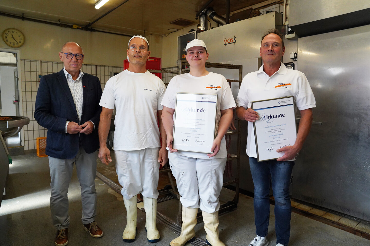 Das Bild zeigt von r.n.l.: Kammervizepräsident Joachim Wagner, Ausbilder Axel Schaub, Lehrling des Monats Georgina Martin und Geschäftsführer Andreas Fuhr bei der Ehrung zum Lehrling des Monats im Arbeitsraum der Metzgerei.
