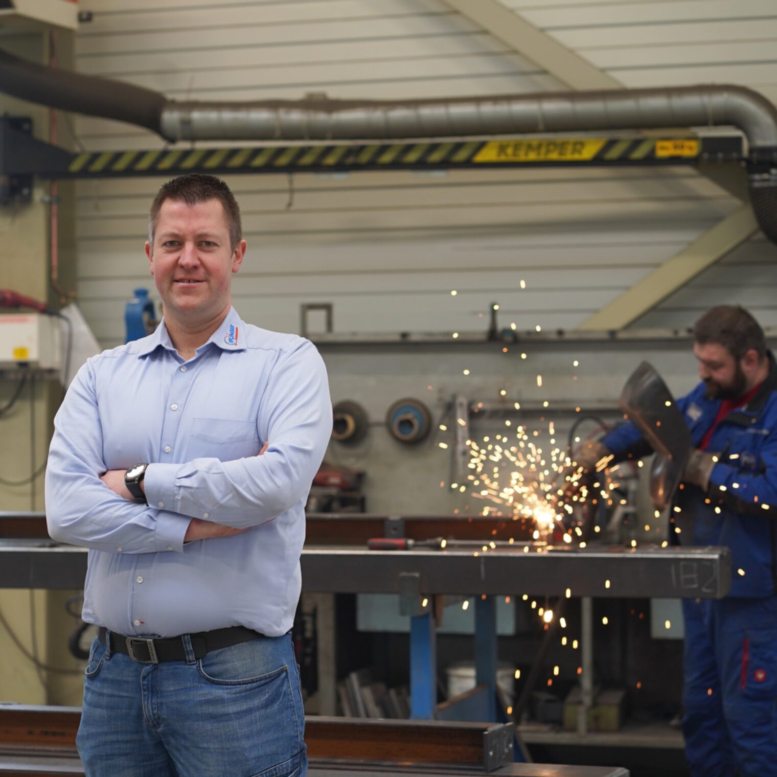 David Iflinger in seiner Metallwerkstatt, ein schweißender Mitarbeiter im Hintergrund.