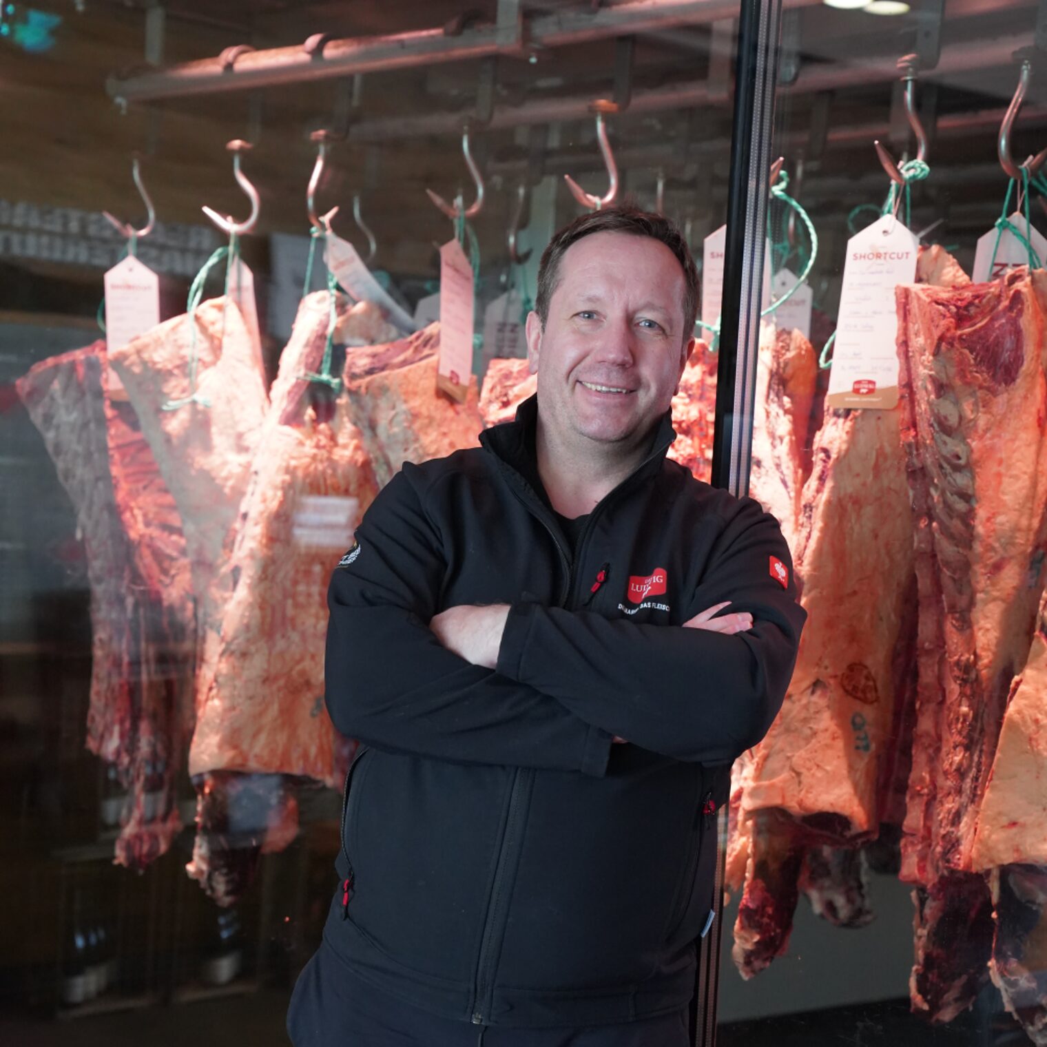 Dirk Ludwig in seinem Verkaufsraum seiner Metzgerei. Im Hintergrund sind in großen Schaufenstern die Fleischhälften zu sehen. 