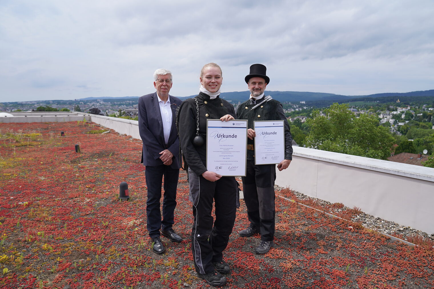 Von links: Hauptgeschäftsführer Bernhard Mundschenk, Lehrling des Monats Mai Hanna Keutner und Schornsteinfegermeister Torsten Schäfer auf dem Flachdach der Handwerkskammer Wiesbaden. Mit Ausblick über die Region.