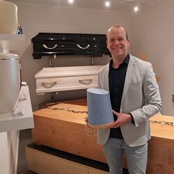 Benedikt Kirchberg steht im Ausstellungsraum seines Bestattungsinstitutes und hält eine Urne in der Hand. 4t