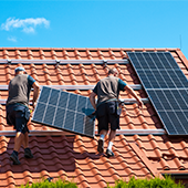 Zwei Handwerker montieren ein Solarpanel auf einem Dach.
