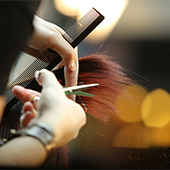 Das Bild zeigt die Hand einer Friseurin mit Kamm, einer Haarsträhne und einer Schere beim Schneiden.