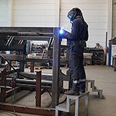 Das Bild zeigt eine große Werkhalle eines Metallbauers und ein Mitarbeiter schweißt gerade an einem Werkstück.