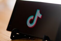 Ein Handy horizontal auf einem Ständer gelegt. Darauf ist das TikTok Logo abgebildet.