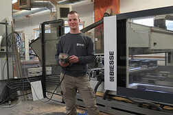 Lehrling des Monats steht in der Tischlerwerkstatt vor einer CNC Maschine und hält deren Fernsteuerung in der Hand.