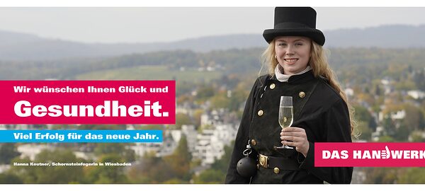 Schornsteinfegerin Hanna Kreutner aus Wiesbaden steht auf dem Dach in ihrer Arbeitskluft und hat ein Glas Sekt in der Hand.