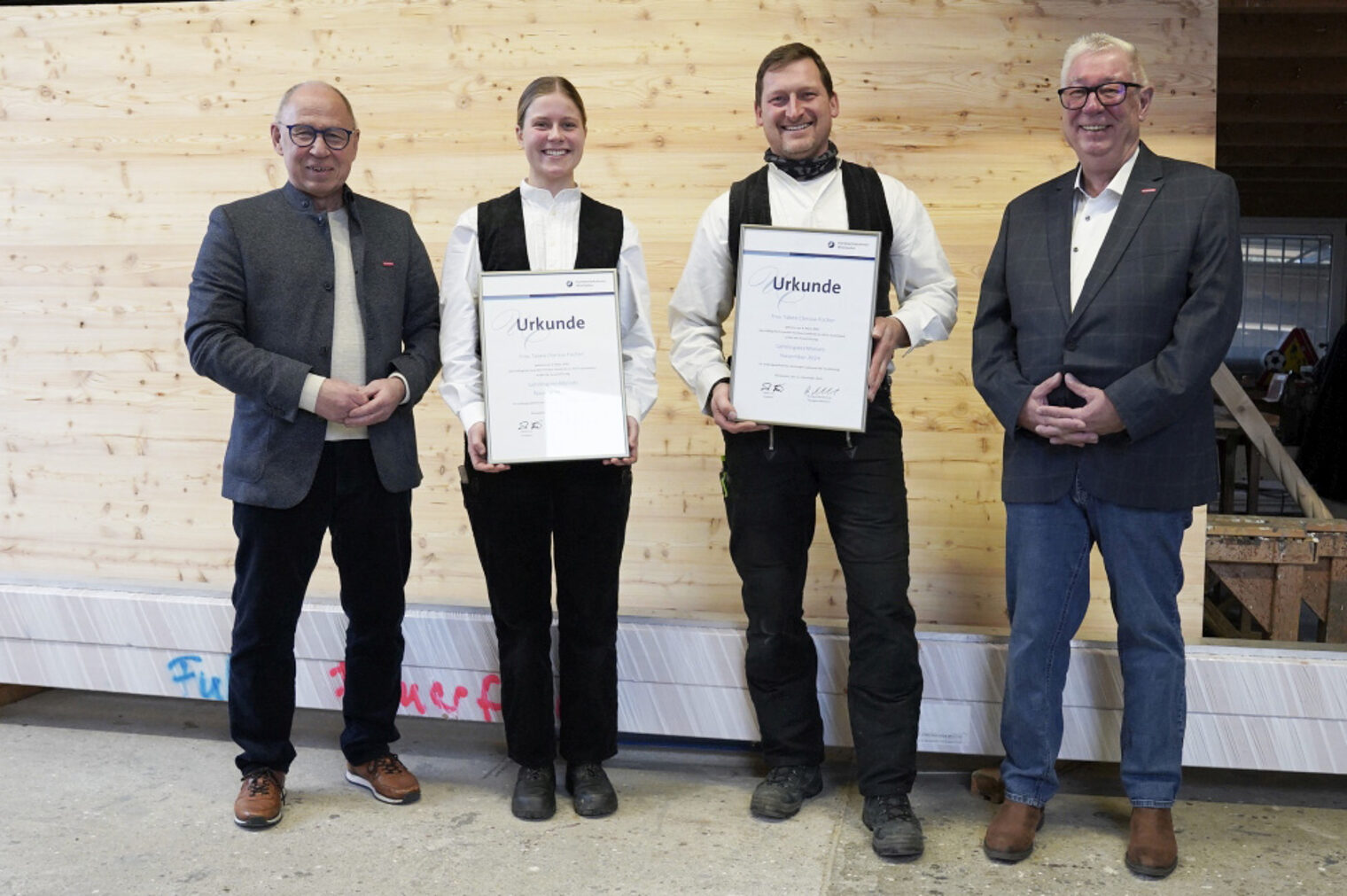Das Bild zeigt von links: Kammervizepräsident Joachim Wagner, Lehrling des Monats Tabea Clarissa Fischer, Zimmermeister Horst Feuerfeil und Kreishandwerksmeister Edwin Giese vor einer Holzwand mit den Urkunden für Frau Fischer und Horst Feuerfeil.