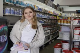 Shalyn Friedrich im Geschäft Farbwerk Völlinger mit einer Farbkarte in der Hand.