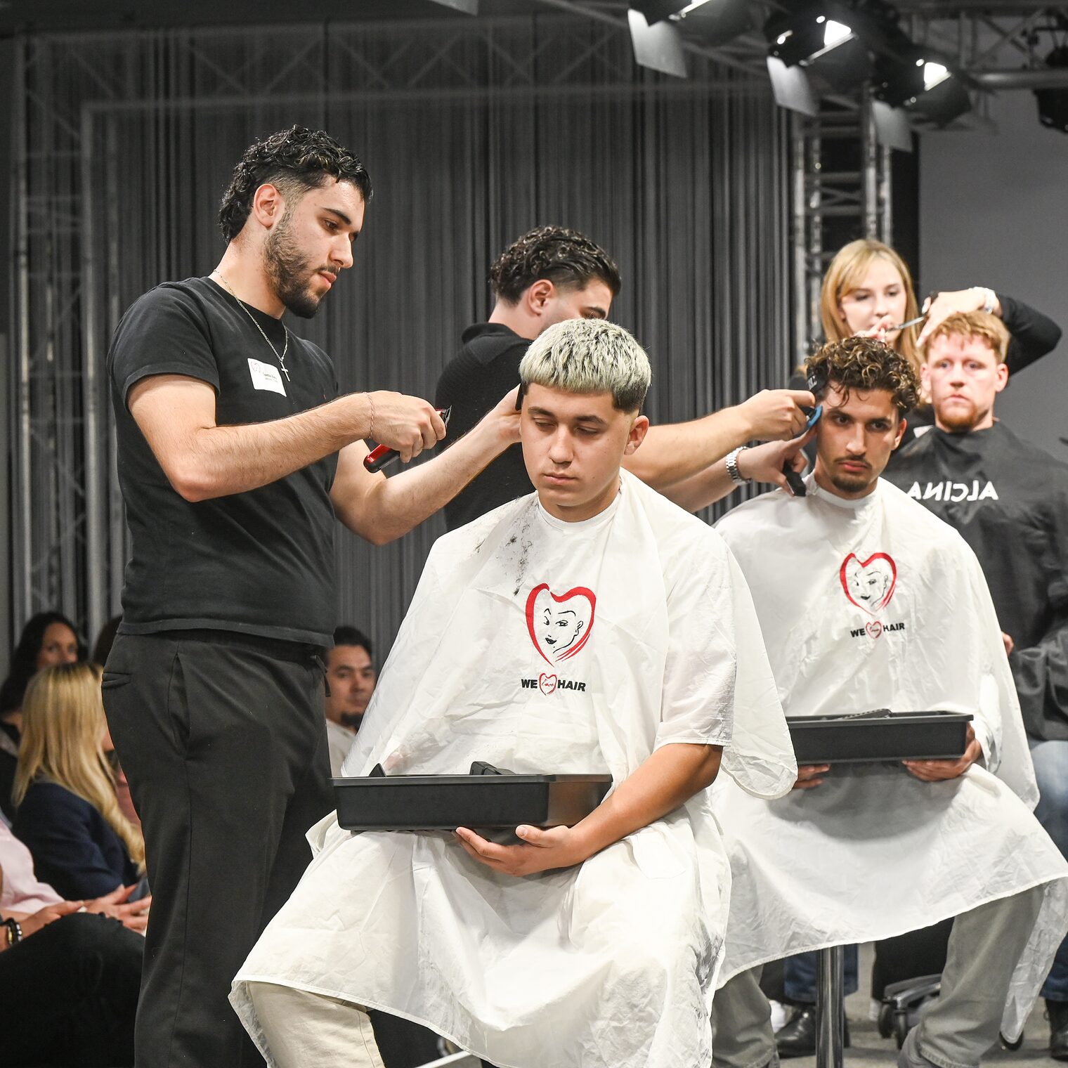 Verschiedene männliche Models bekommen die Haare auf der Bühne geschnitten.